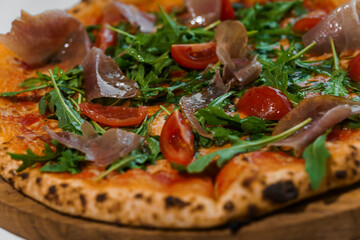 Pepperoni pizza with arugula and prosciutto. Meat pizza with cheese, cherry tomatoes and fresh arugula on a white background