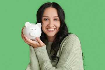 Pretty young woman with piggy bank on green background