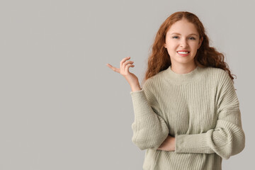 Portrait of ashamed young woman pointing at something on grey background