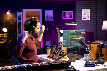 Please happy songwriter creating new music on daw software, using headset to listen to the final product in home studio. Young music producer editing audio files recordings on pc.