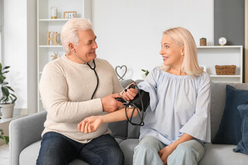 Mature man measuring blood pressure of his wife at home