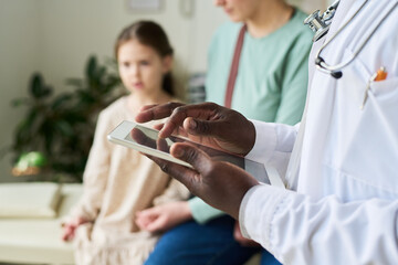 Medical professional checking patient records on tablet while young female patient sitting on bench...