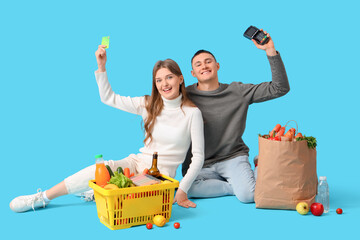 Young couple with credit card, payment terminal and foods on blue background. Shopping concept