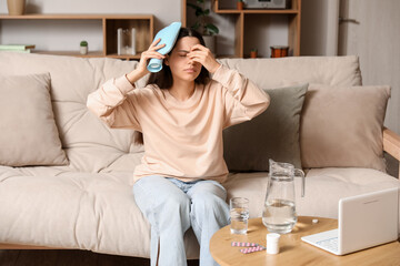 Young woman suffering from headache with heating pad at home