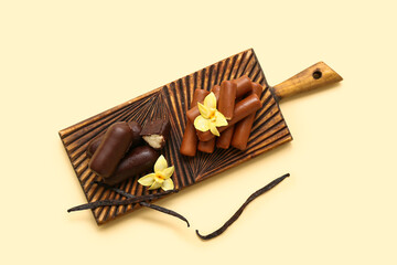 Wooden board with tasty chocolate glazed curd snacks with vanilla flavor on light yellow background