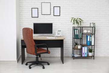 Interior of stylish office with workplace, armchair, modern computer and shelving unit