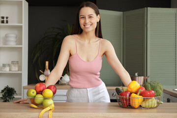 Obraz premium Beautiful young happy woman with measuring tape, bowls of fresh fruits and vegetables in kitchen. Weight loss concept
