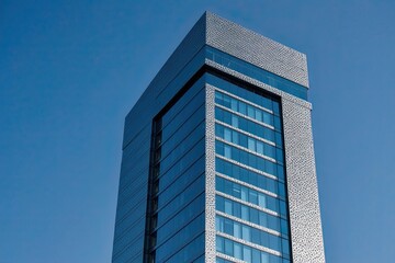Obraz premium Modern Business Tower Featuring Textured Glass and Distinctive Windows Set Against a Blue Sky