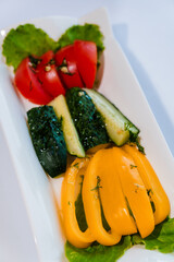 Fresh vegetables tomatoes, yellow pepper and cucumber on a white plate on a white background