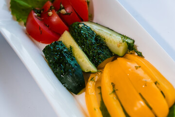 Fresh vegetables tomatoes, yellow pepper and cucumber on a white plate on a white background