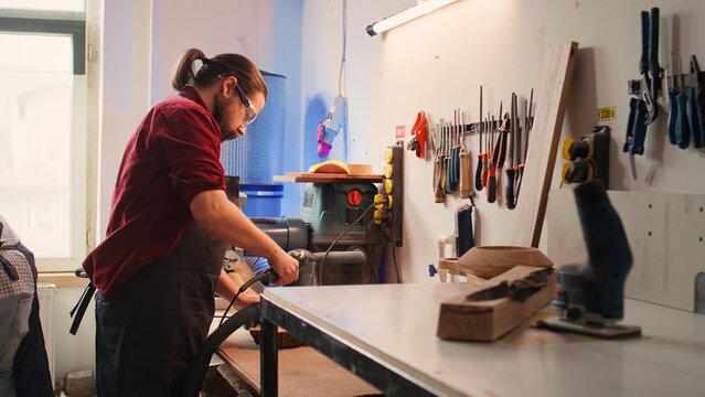 Carpenter collaborating with apprentice, using orbital sander with fine sandpaper to achieve refined finish. Manufacturer and BIPOC colleague using angle grinder on wood block, camera B