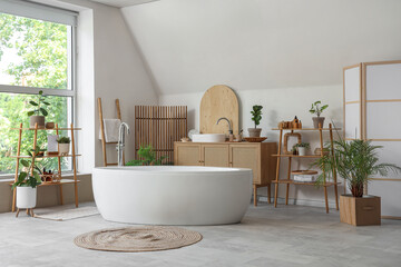 Interior of light bathroom with folding screen, bathtub and houseplants