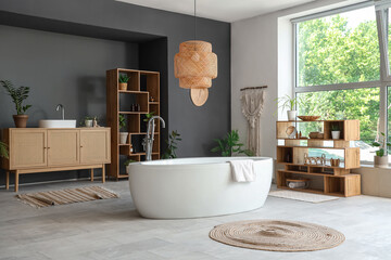 Bathtub, chest of drawers, wooden shelving unit and houseplants in modern bathroom