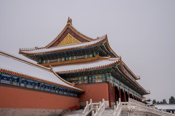 A traditional Chinese palace building with ornate, tiered roofs covered in snow. The structure...