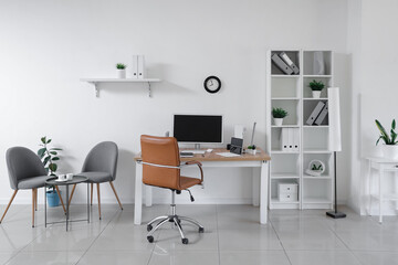 Stylish interior of light office with workplace, modern computer, shelving unit and armchair