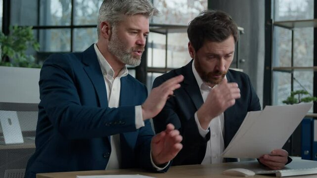 Two Caucasian men businessmen business partners argue in office meeting discussing bad project conflict failure failed contract mistake in financial papers illegal documents dissatisfied work result