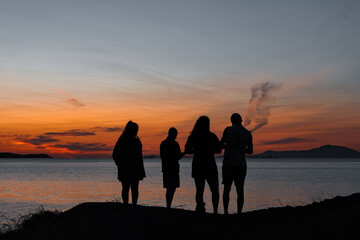 silhouette of 4 people at the shoreline at sunset