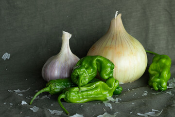 Still life of garlic, peppers, and an onion on an olive green background.