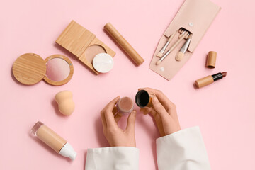 Female hands with different cosmetic products and makeup brushes on pink background