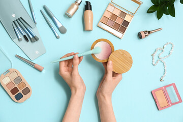 Female hands with different decorative cosmetics and makeup brushes on color background