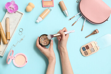 Female hands with powder pearls, makeup brush and different cosmetics on color background