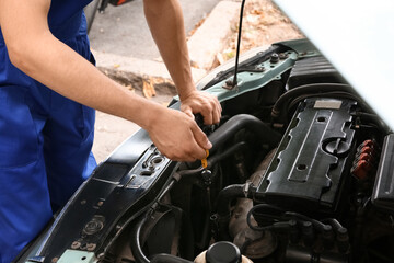 Fototapeta premium Male mechanic checking level of car oil outdoors, closeup