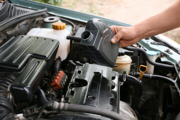 Male mechanic pouring car oil into engine outdoors, closeup