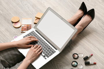 Fototapeta premium Makeup artist with cosmetic products using laptop on wooden floor, closeup