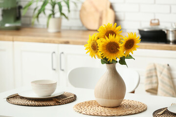 Vase with sunflowers on served dining table in kitchen. Closeup