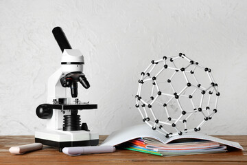 Modern microscope with copybooks and molecular model on wooden table against white grunge background