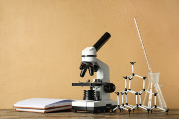 Modern microscope with chemical flask, molecular model and book on wooden table against beige...