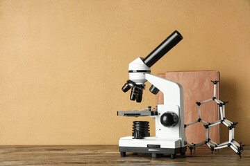 Modern microscope with molecular model and book on wooden table against beige background