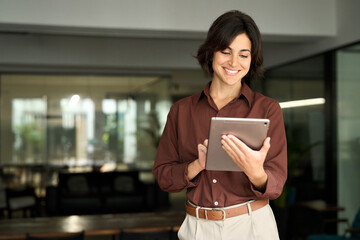 Smiling young adult Hispanic businesswoman leader or entrepreneur, company worker using tablet at...