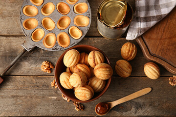 Composition with tasty walnut shaped cookies, boiled condensed milk and baking form on wooden background