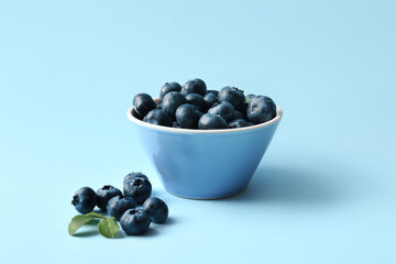 Bowl with fresh ripe blueberry on blue background, closeup