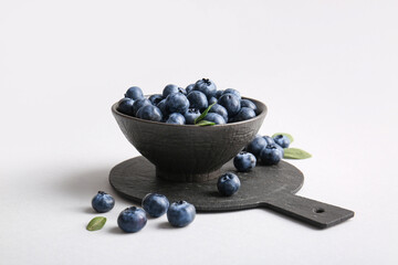 Cutting board and bowl with fresh ripe blueberry on white background, closeup