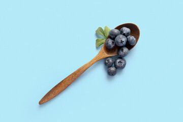 Wooden spoon with fresh ripe blueberry on blue background