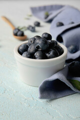 Napkin and bowl of ripe blueberry on pale blue background, closeup