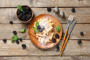 Delicious Belgian waffles with blackberries and sugar powder on plate on wooden background. Top view