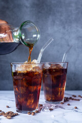cold brew coffee pouring from bottle in to glass with iced on white marble floor.
