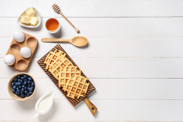 Delicious Belgian waffles with blueberries and honey on board on white wooden background. Top view