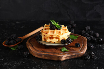 Delicious Belgian waffles with blackberries on board on black background