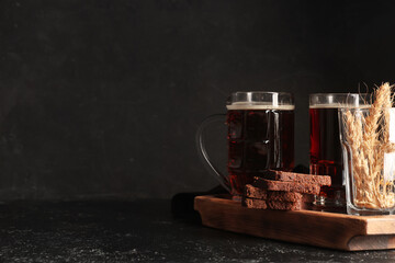 Glasses of fresh kvass with slices of bread and wheat on black background