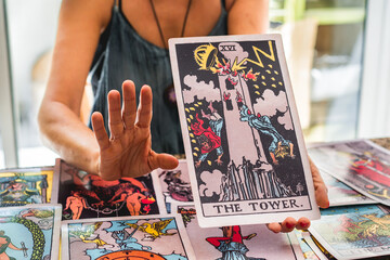 Tarot reader showing the giant Tarot card The Tower while raising her hand as if to say Wait