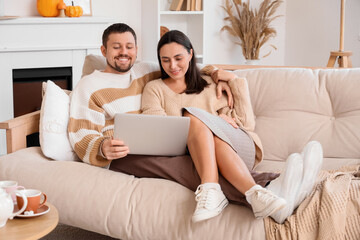 Happy young couple with laptop sitting at home on autumn day