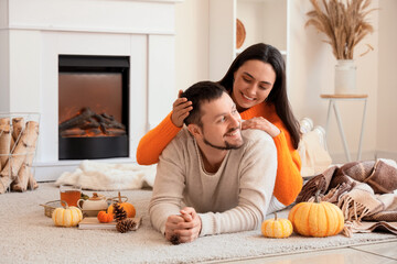 Happy young couple with autumn decor lying near fireplace at home