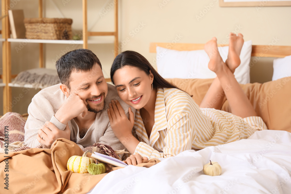 Wall mural happy young couple with pumpkins reading book and lying in bedroom at home on autumn day