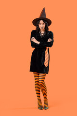 Beautiful young angry woman dressed as witch for Halloween on orange background