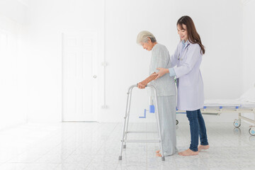 Asian female doctor assisting elderly patient with walker in hospital. Healthcare professional...