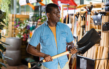 Fototapeta premium Portrait of a concentrated african american man choosing working tools in the horticultural market